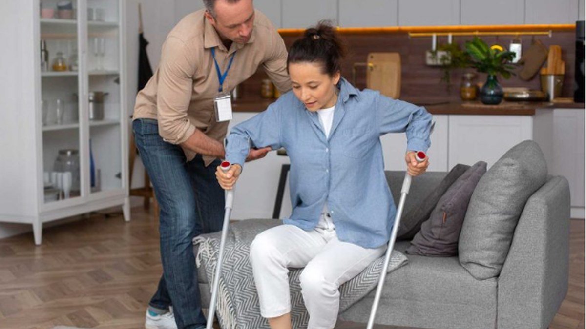 A support worker helping a participant walk with crutches in their own living room